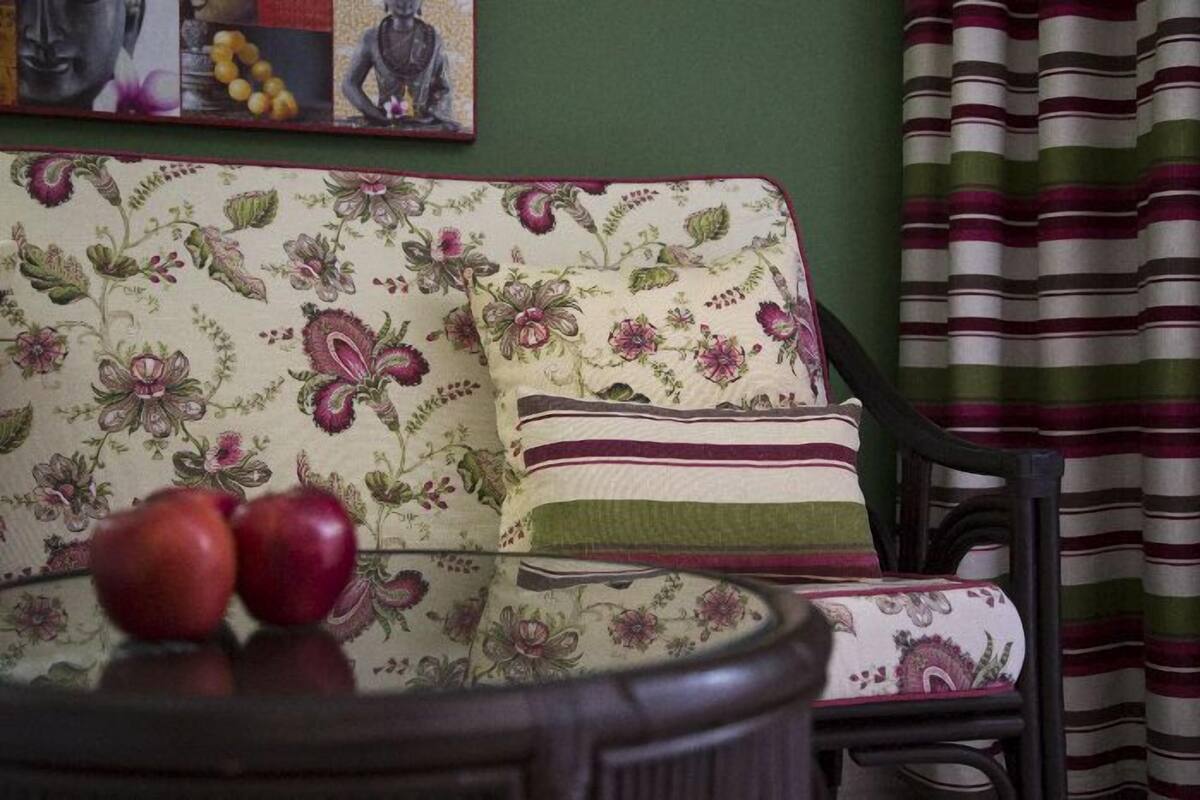 Un canapé à motifs floraux avec un coussin, une chaise et une table sur laquelle se trouvent des pommes.
