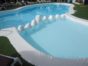 En swimmingpool med hvide sten arrangeret i en række, omgivet af kunstgræs og hvide liggestole.