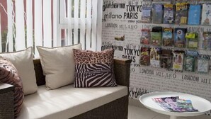 Een moderne woonkamer met een bank, kussens, een ronde tafel en een muur versierd met ansichtkaarten met reisafbeeldingen.