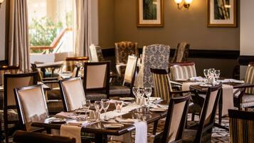 A restaurant with tables set for dining, chairs, and a view of greenery outside.