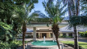 Un patio con una fuente, palmeras y un edificio de techo plano.