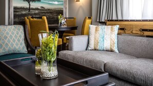 Una sala de estar moderna con un sofá gris, sillas amarillas y una mesa de centro de madera con un jarrón de flores.