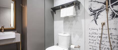 A modern bathroom with a glass shower enclosure, a white toilet, a gold-framed mirror, and a marble-tiled wall with a leaf pattern.
