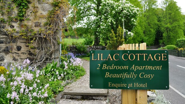 A sign for Lilac Cottage, a 2-bedroom apartment, with a garden in the background. - Moulin Hotel (Pitlochry)