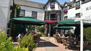 An outdoor seating area with tables and chairs, surrounded by white buildings with black trim and flower boxes. - Moulin Hotel (Pitlochry)