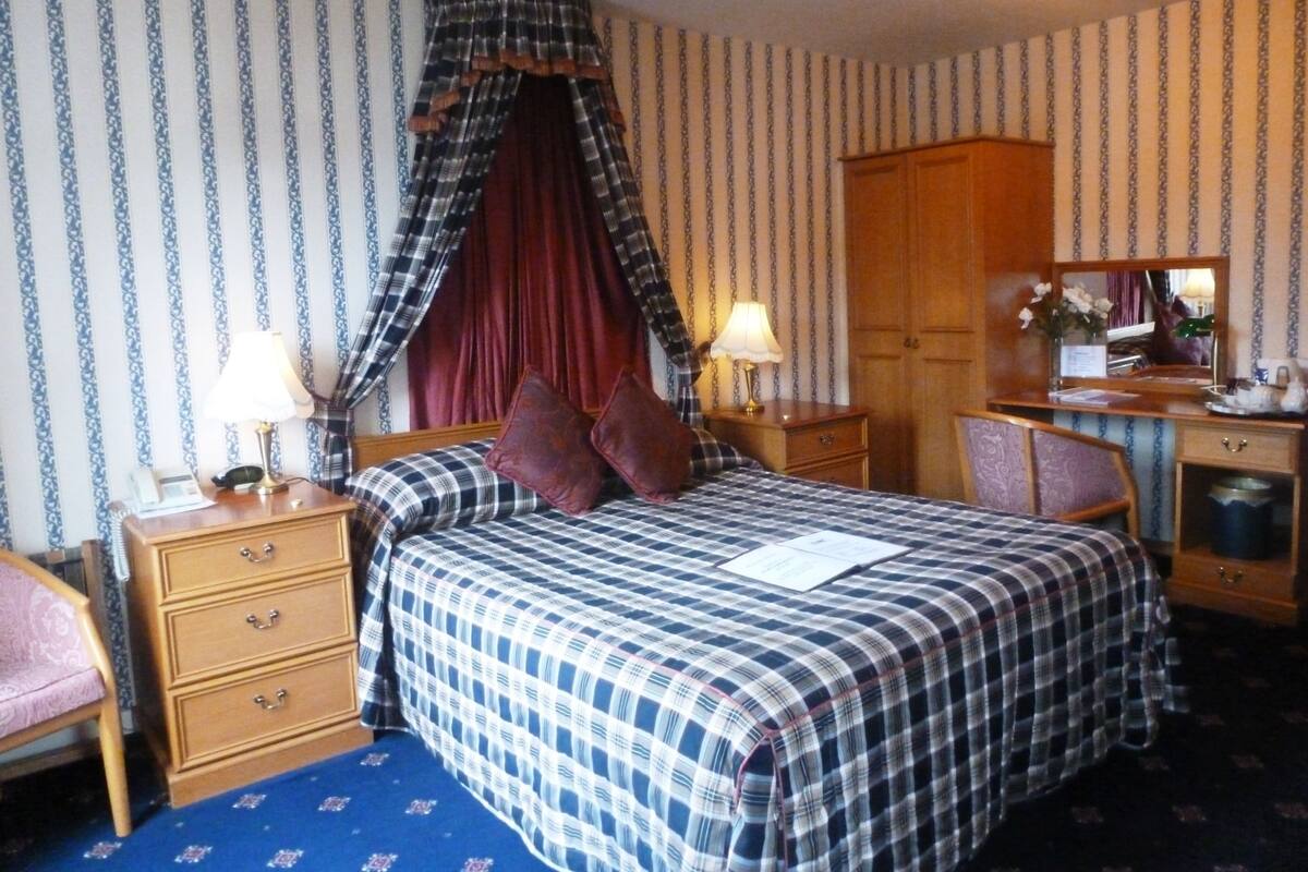 A hotel room with a bed, two bedside tables, a desk, a chair, a wardrobe, and a mirror.