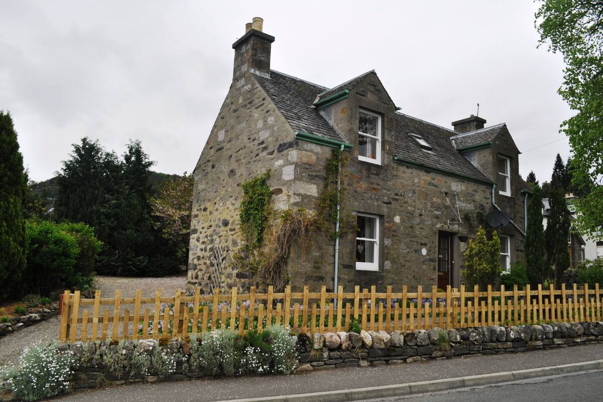 A stone house with a wooden fence, a stone wall, and a gravel driveway.