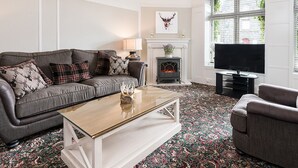 A living room with a grey sofa, a coffee table, a fireplace, and a television. - Moulin Hotel (Pitlochry)