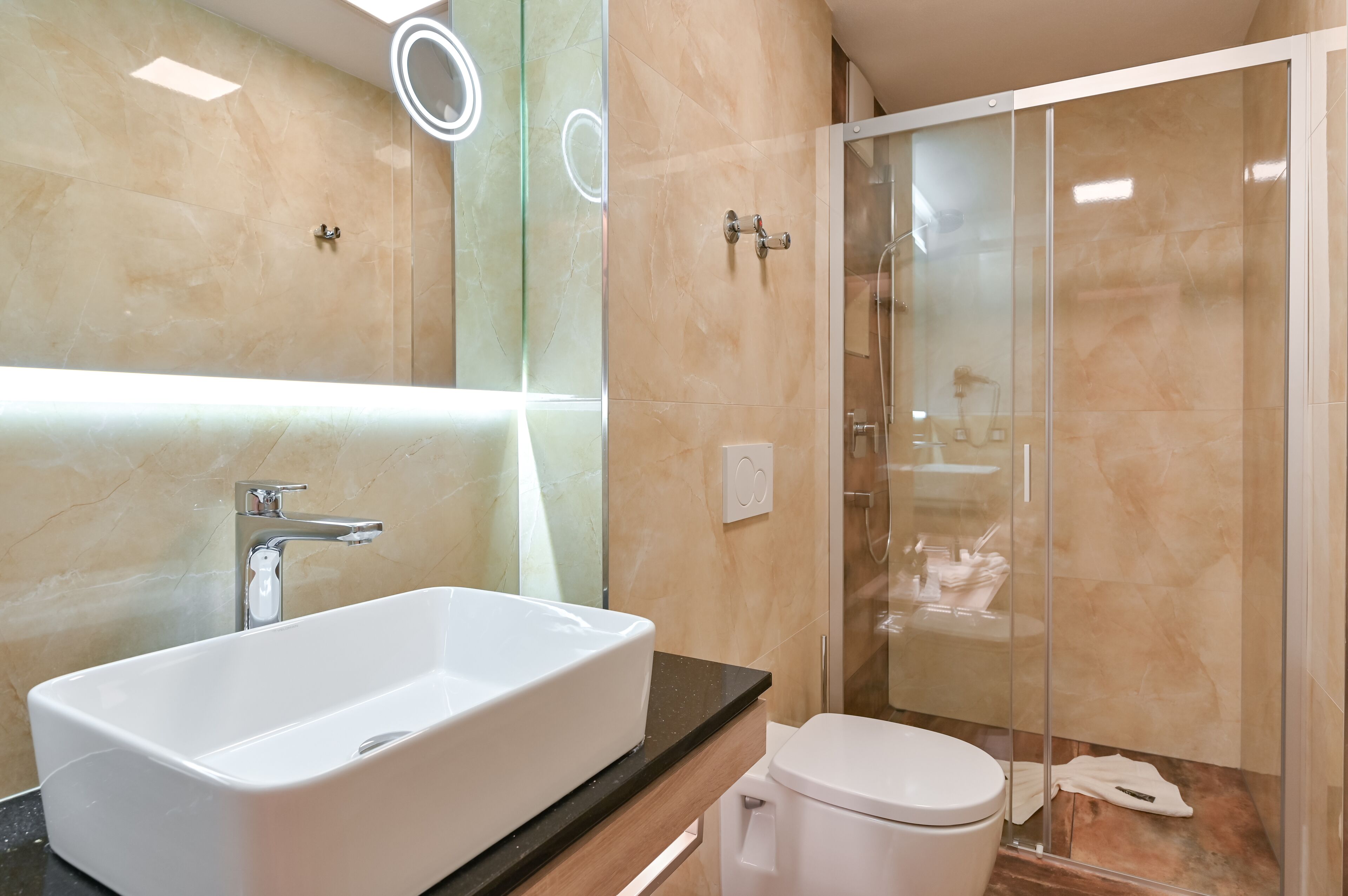 Un baño moderno con un lavamanos blanco grande, un inodoro y una ducha con mampara de vidrio.