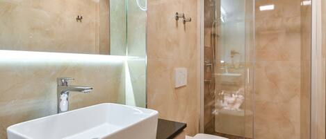 Un baño moderno con un lavamanos blanco grande, un inodoro y una ducha con mampara de vidrio.