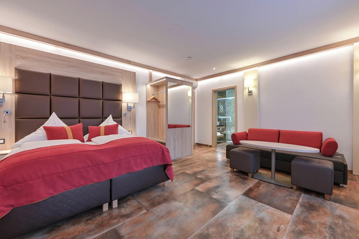 A modern hotel room with a large bed, a seating area with a table, and a walk-in closet.