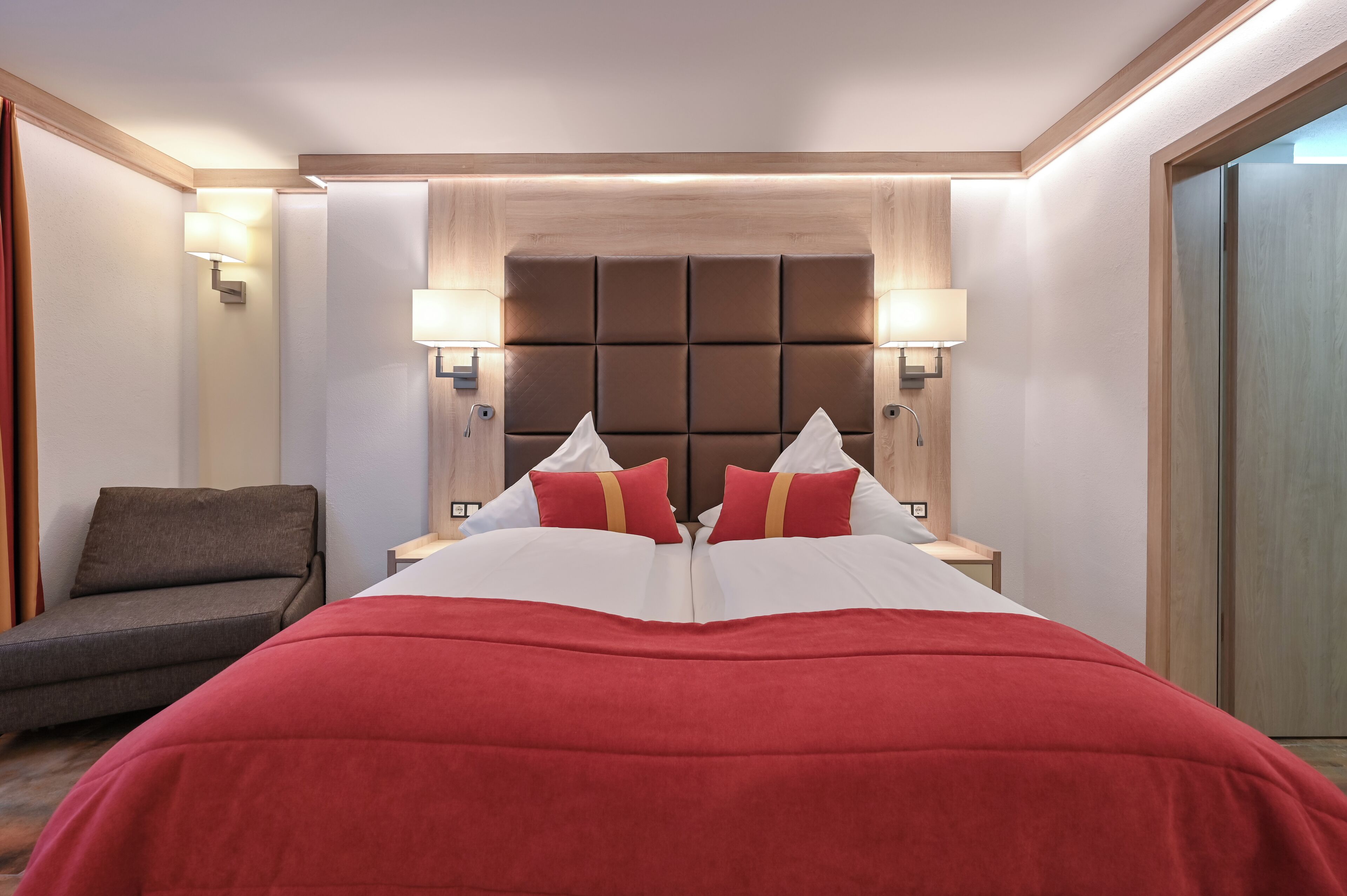 Une chambre d’hôtel avec un grand lit, deux lampes de chevet, une tête de lit et un petit canapé.