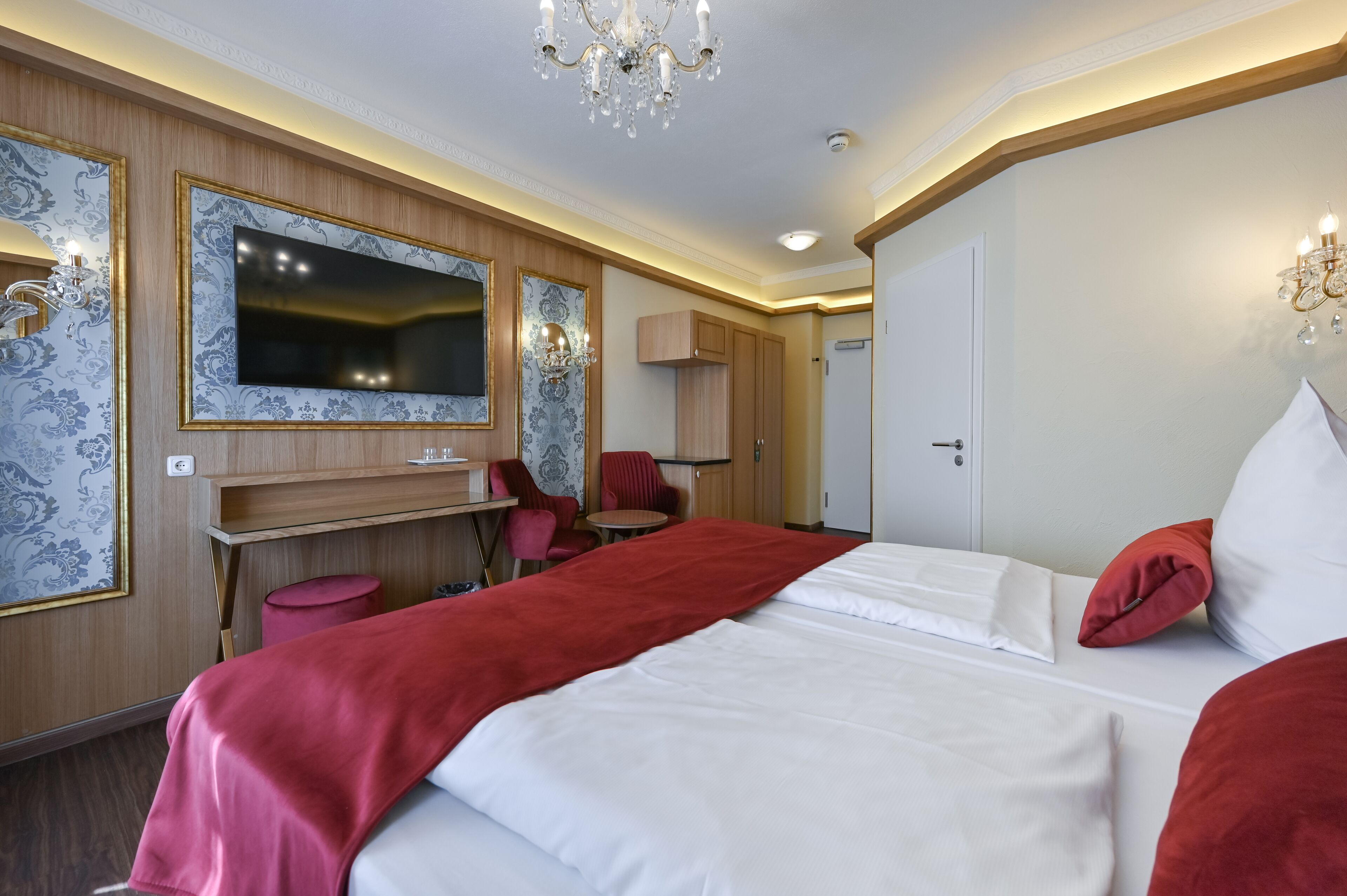 Habitación de hotel con una cama grande, un escritorio, una silla, un televisor y una araña.