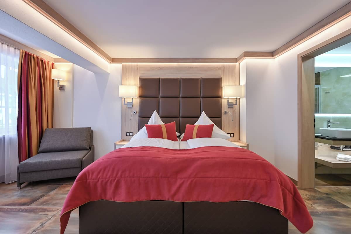 A hotel room with a large bed, a chair, a nightstand, and a bathroom visible through an open door.