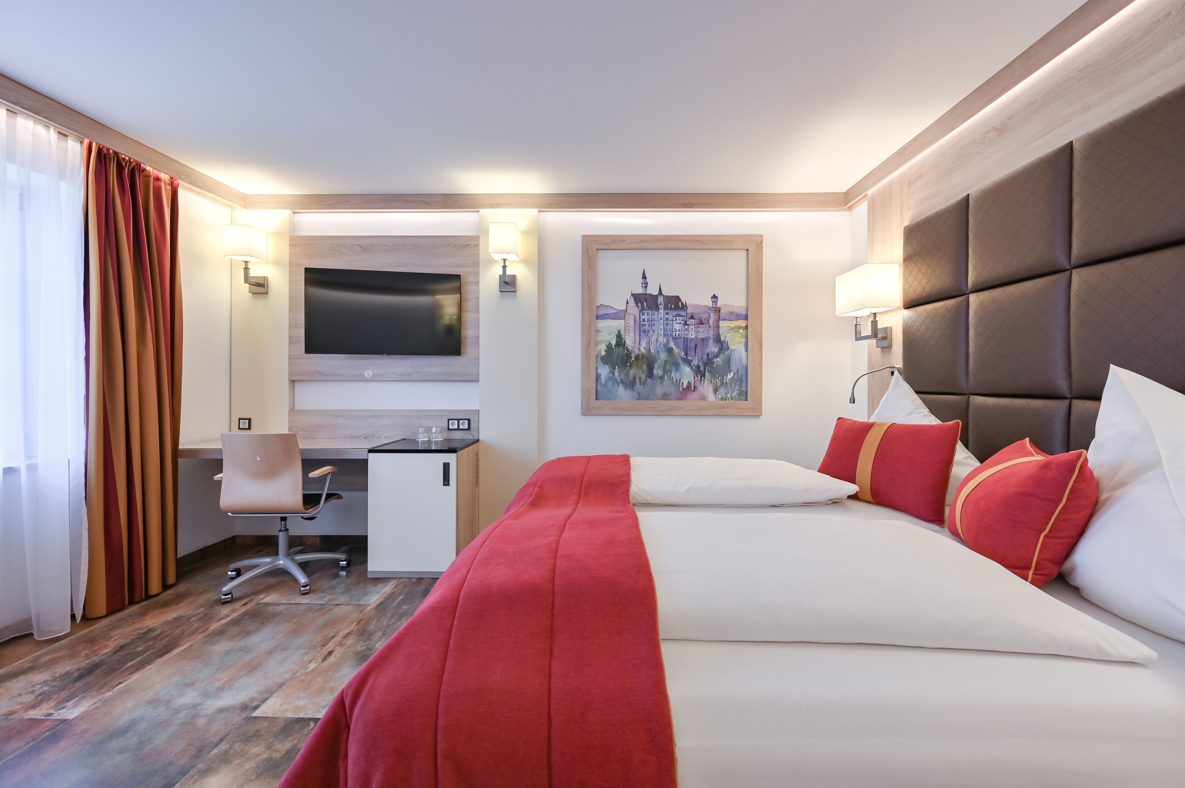 A hotel room with a bed, a desk, a chair, a TV, and a painting on the wall.