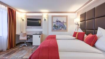 A hotel room with a bed, a desk, a chair, a TV, and a painting on the wall.