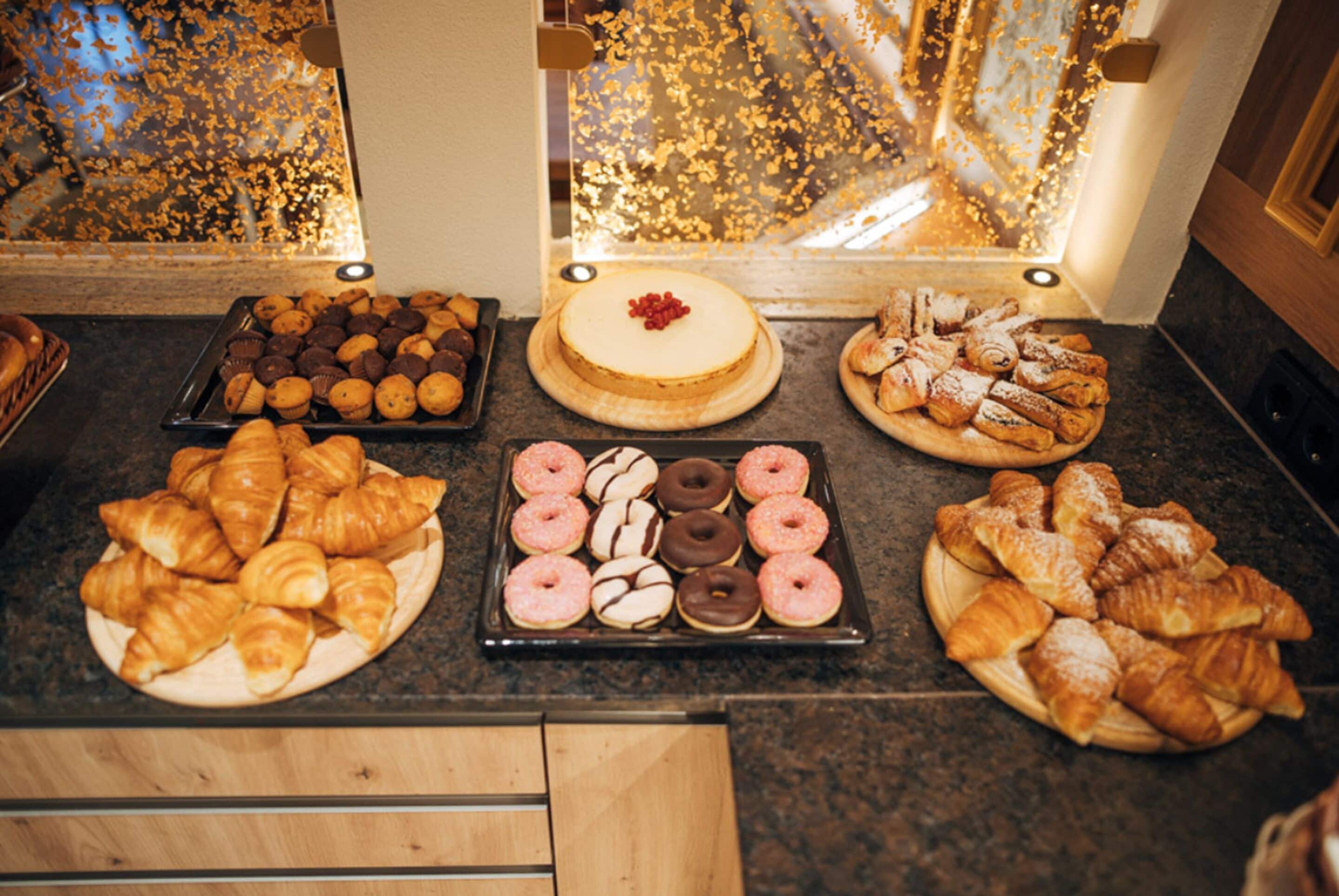 A variety of pastries displayed on a counter, including croissants, donuts, and a cake with a cherry on top.