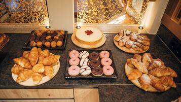 A variety of pastries displayed on a counter, including croissants, donuts, and a cake with a cherry on top.