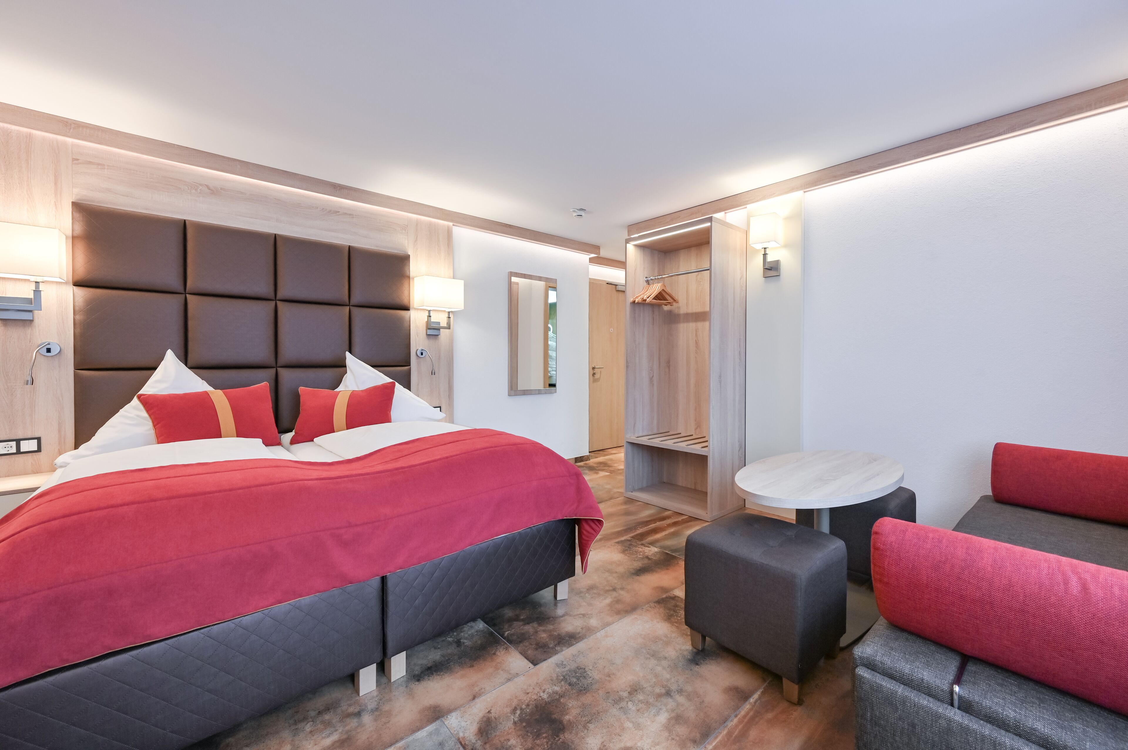 Ein modernes Hotelzimmer mit einem großen Bett, einer Sitzecke, einem kleinen Tisch und einem begehbaren Kleiderschrank.