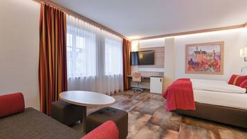 A hotel room with a bed, a desk, a TV, and a painting.
