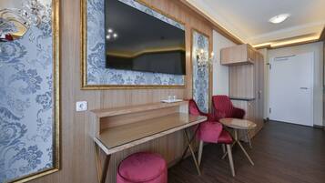 Una habitación moderna con un televisor de pantalla plana grande montado en una pared con papel tapiz decorativo, un escritorio de madera, una silla roja y un pequeño otoman.