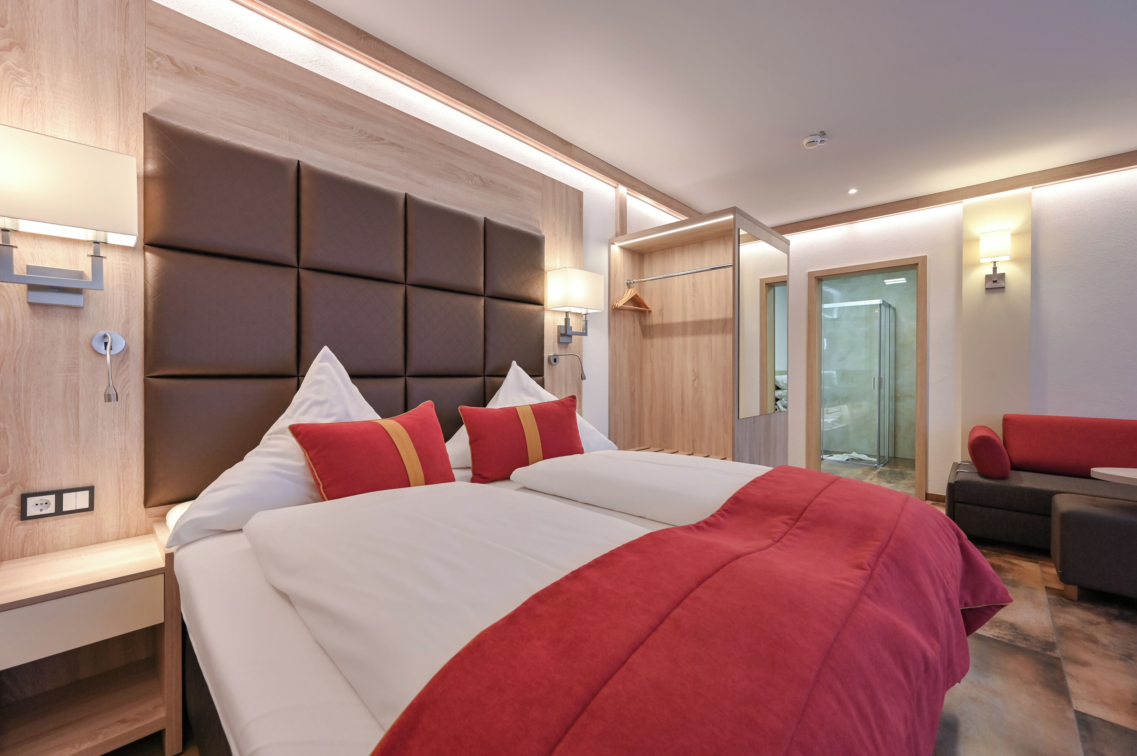 Une chambre d’hôtel moderne dotée d’un grand lit, d’une table de chevet, d’une armoire et d’un coin salon avec un canapé rouge.