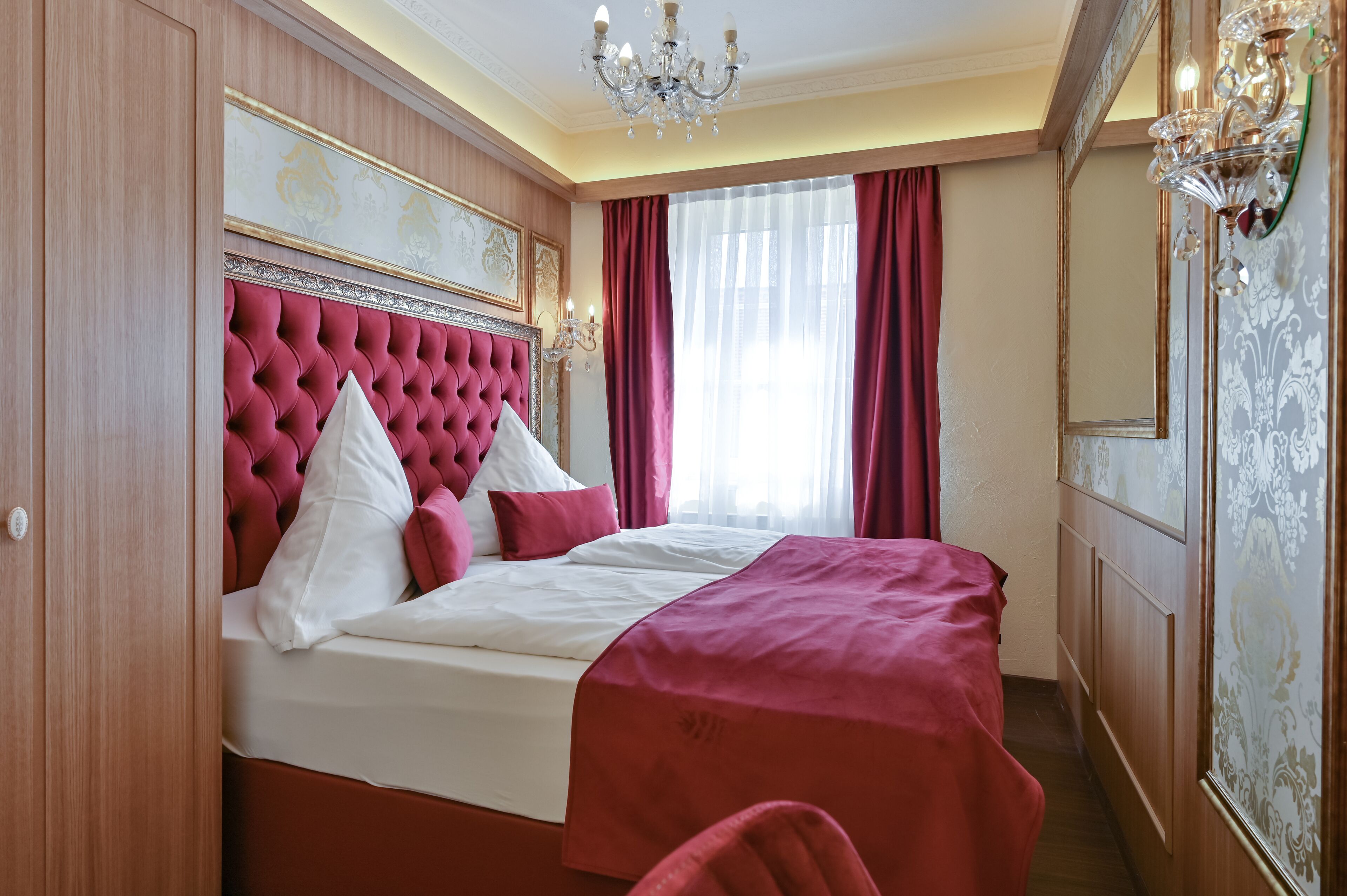 A bedroom with a tufted headboard, a large bed with red and white bedding, and a chandelier.