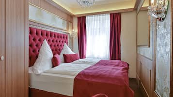 Un dormitorio con cabecera capitonada, una cama grande con ropa de cama roja y blanca, y una araña.