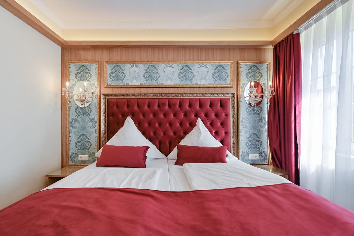 A hotel room with a large bed, red and white bedding, a tufted headboard, and decorative wall panels.
