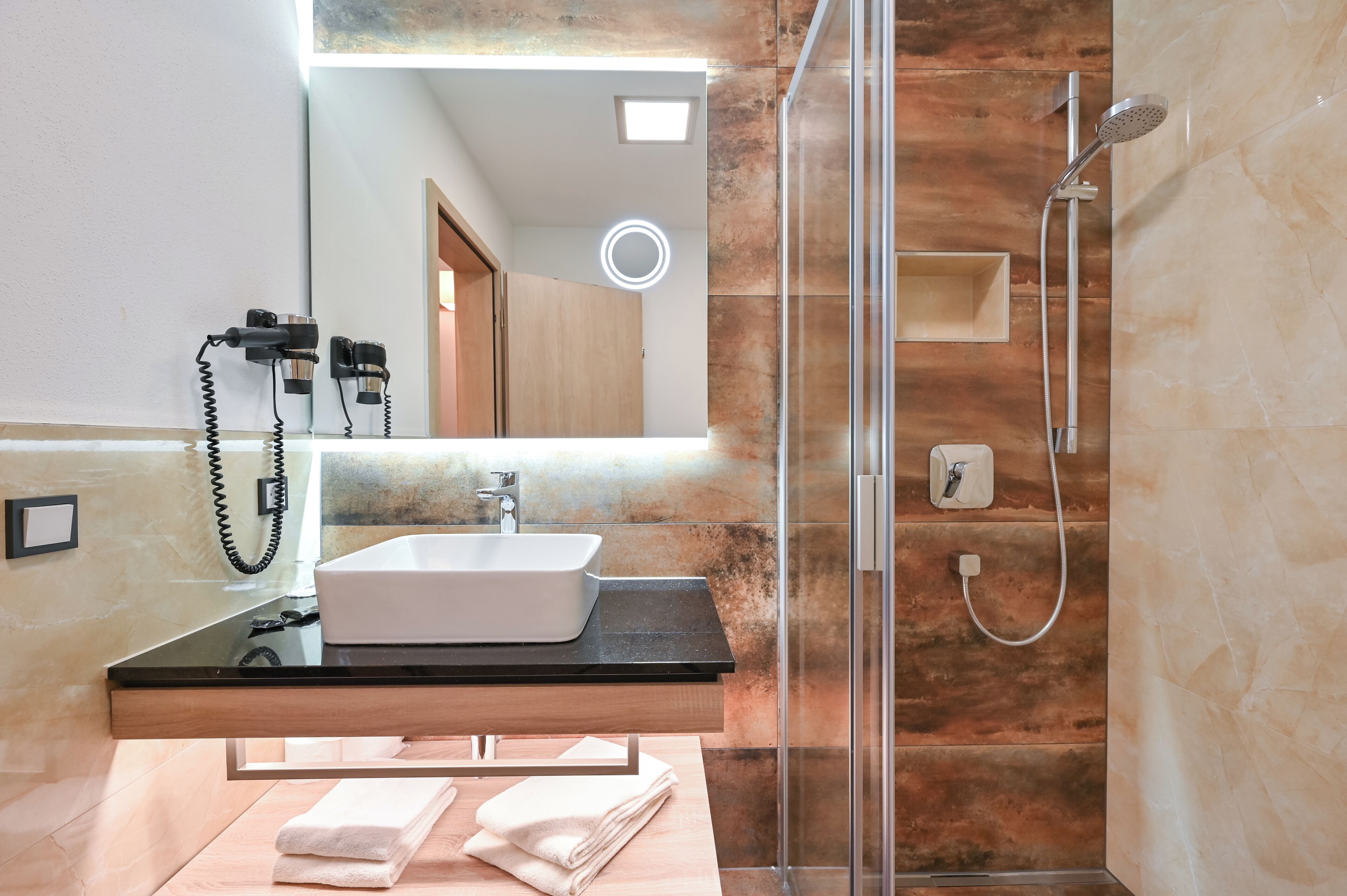 Une salle de bain moderne avec une douche à l’italienne en verre, un plan de toilette noir et un lavabo blanc.