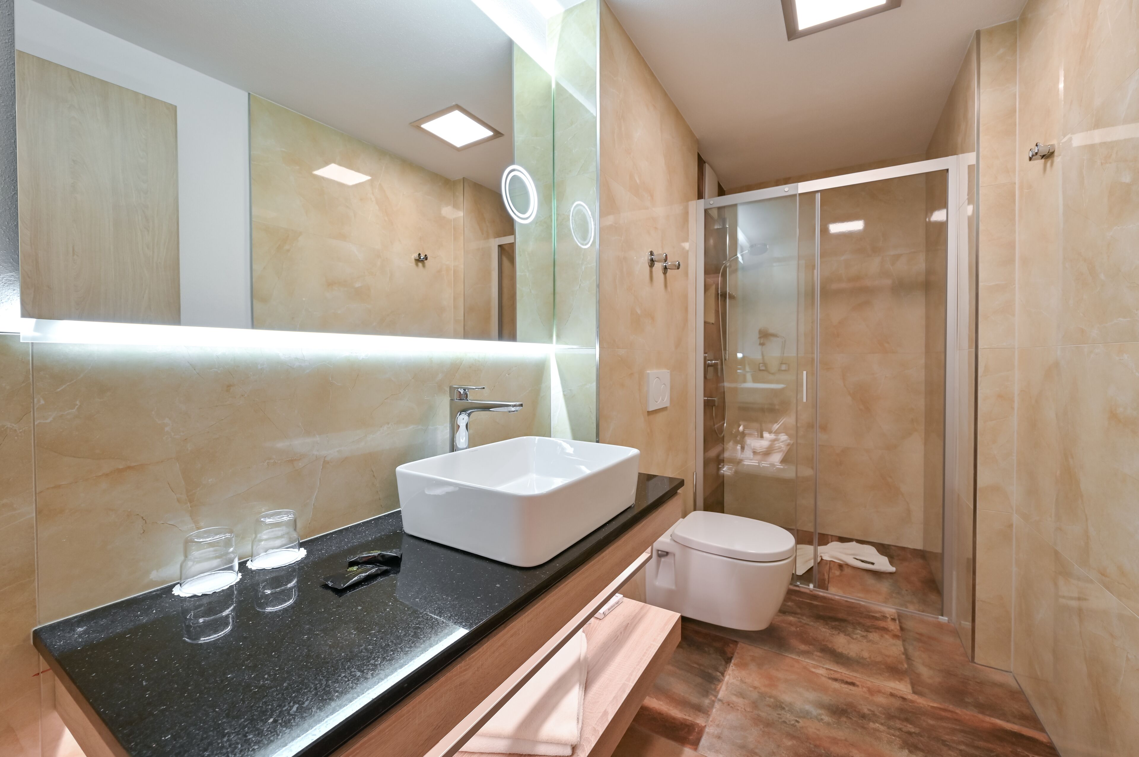 Un baño moderno con un espejo grande, un lavamanos blanco y una ducha con mampara de vidrio.