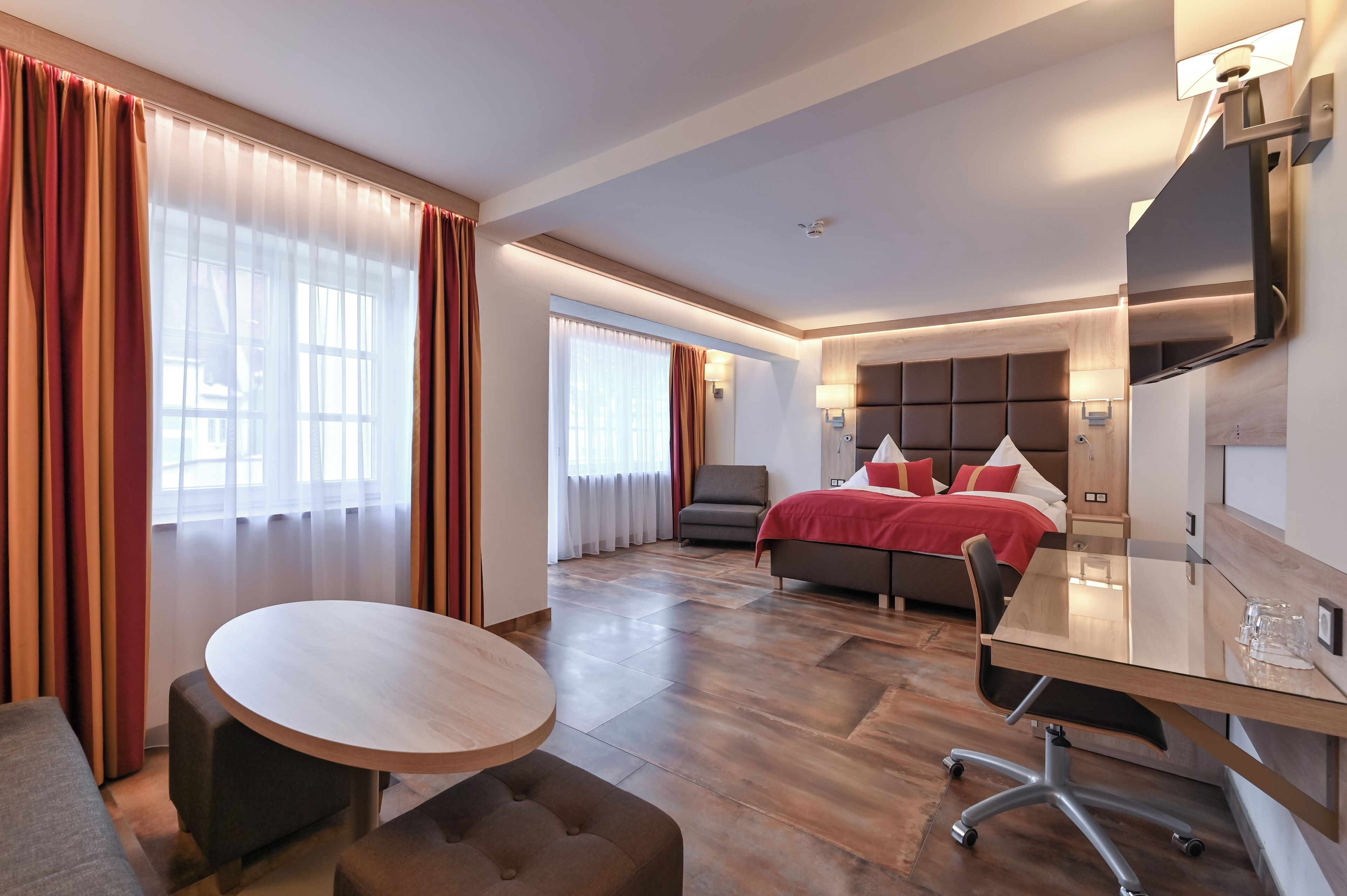 A modern hotel room with a large bed, a desk with a chair, a round table, and a sofa.