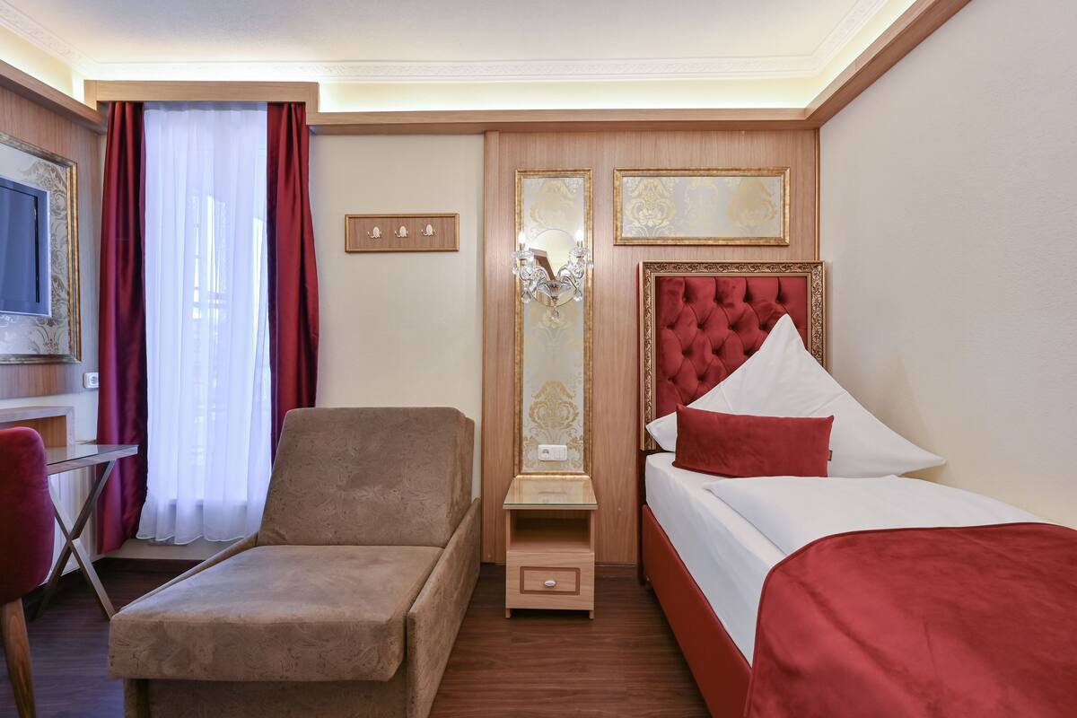 A hotel room with a bed, a chair, a desk, and a mirror.