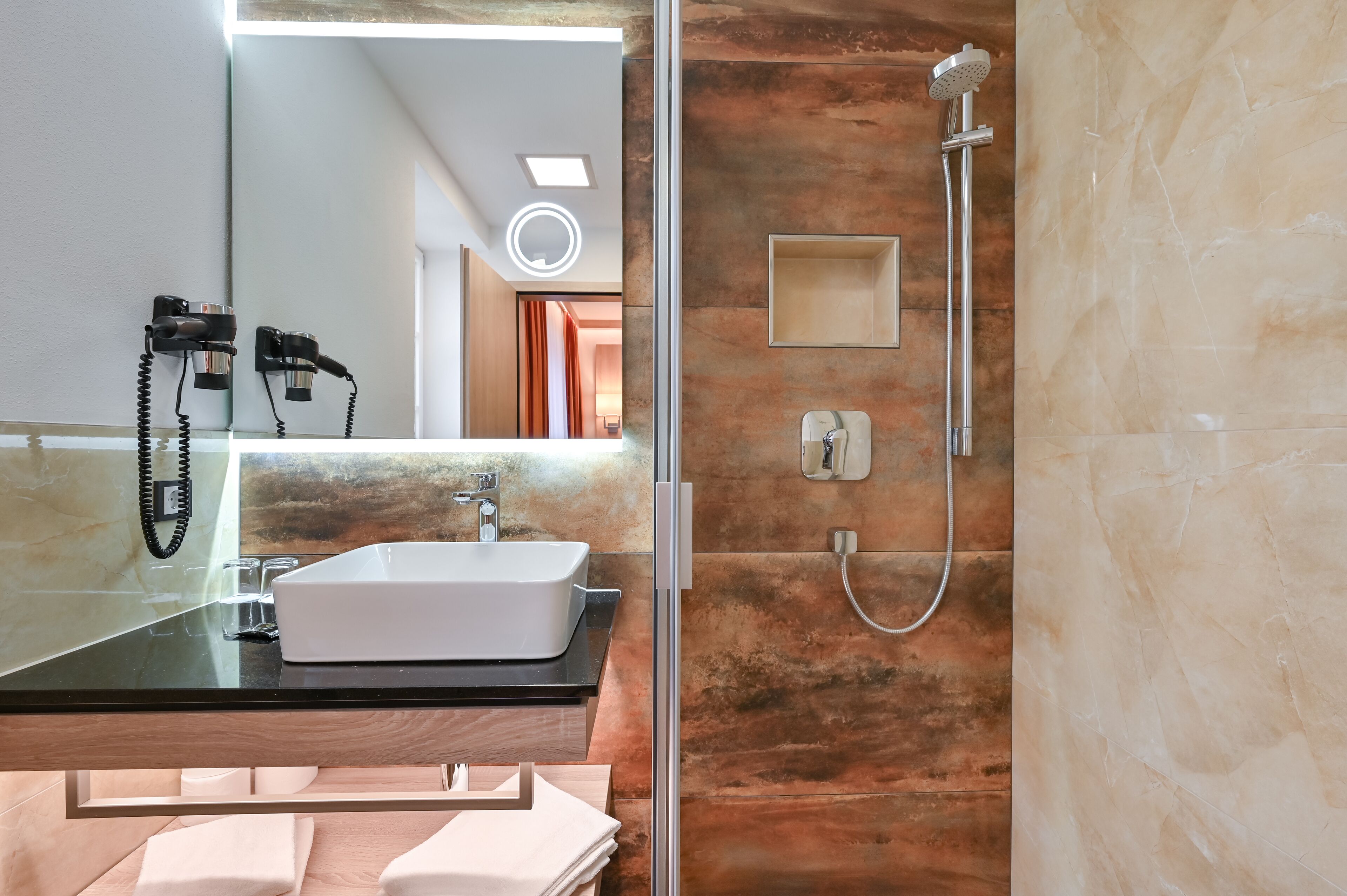 A modern bathroom with a glass-enclosed sink, a handheld showerhead, and a mirror with a light.