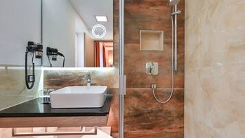 Un baño moderno con un lavamanos con cubierta de vidrio, un cabezal de ducha de mano y un espejo con luz.