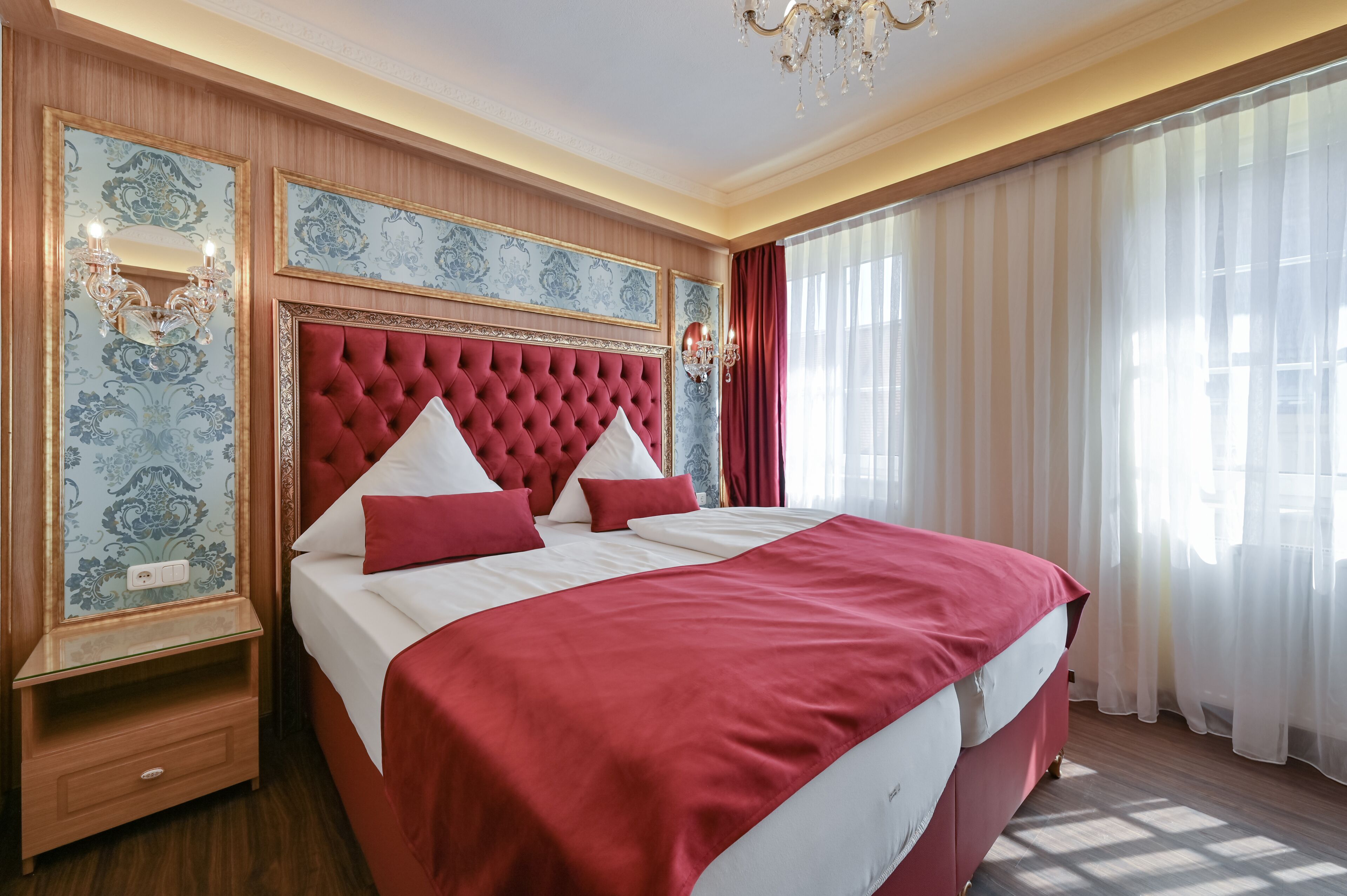 A large bed with a tufted headboard, red bedding, and two bedside lamps.