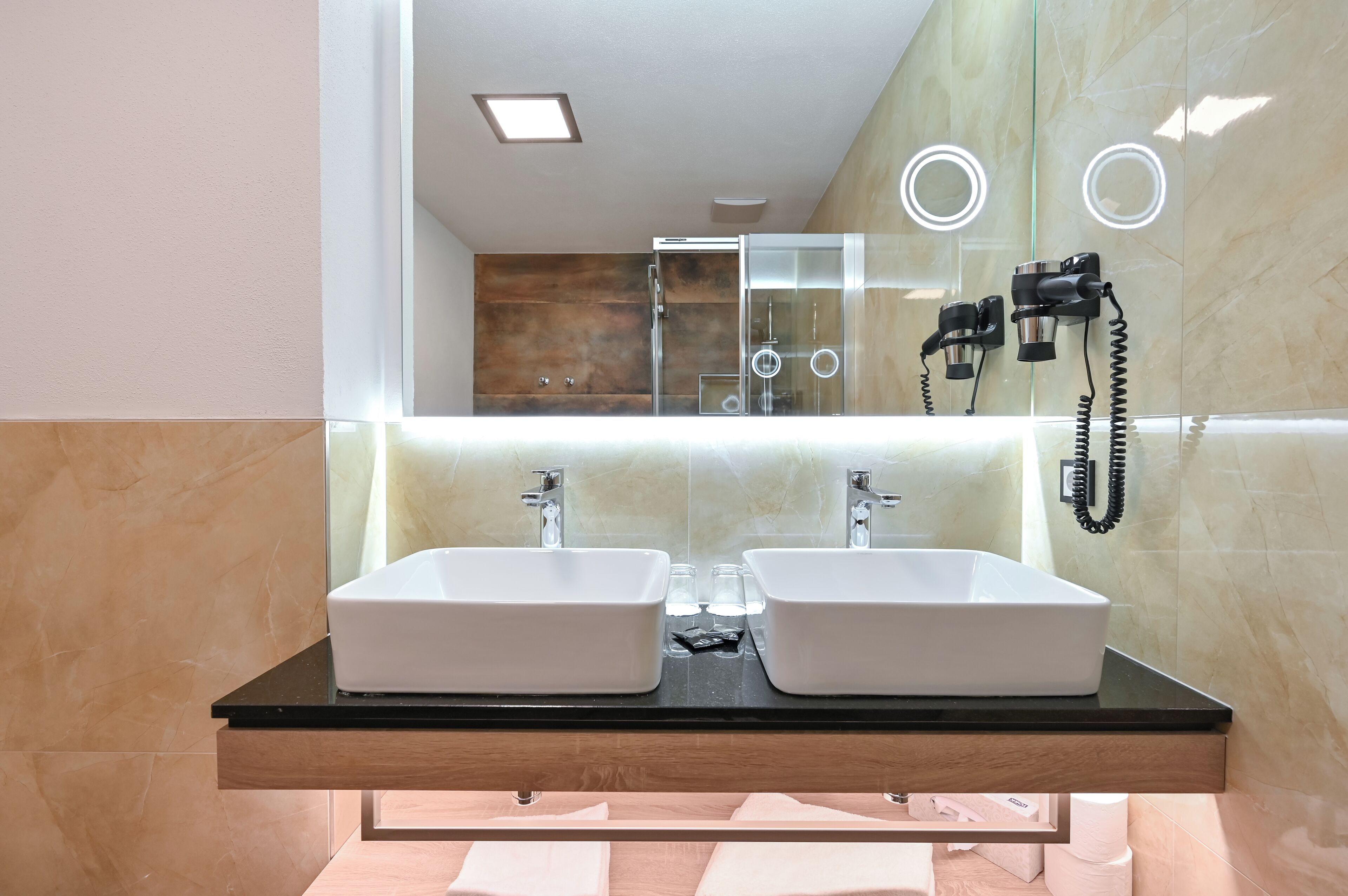 Un baño moderno con dos lavamanos blancos, un espejo y una cabina de ducha de vidrio.