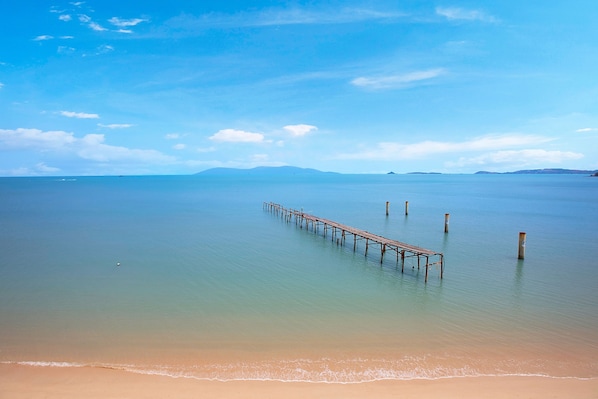 A beach with a wooden pier extending into calm waters, surrounded by clear skies.