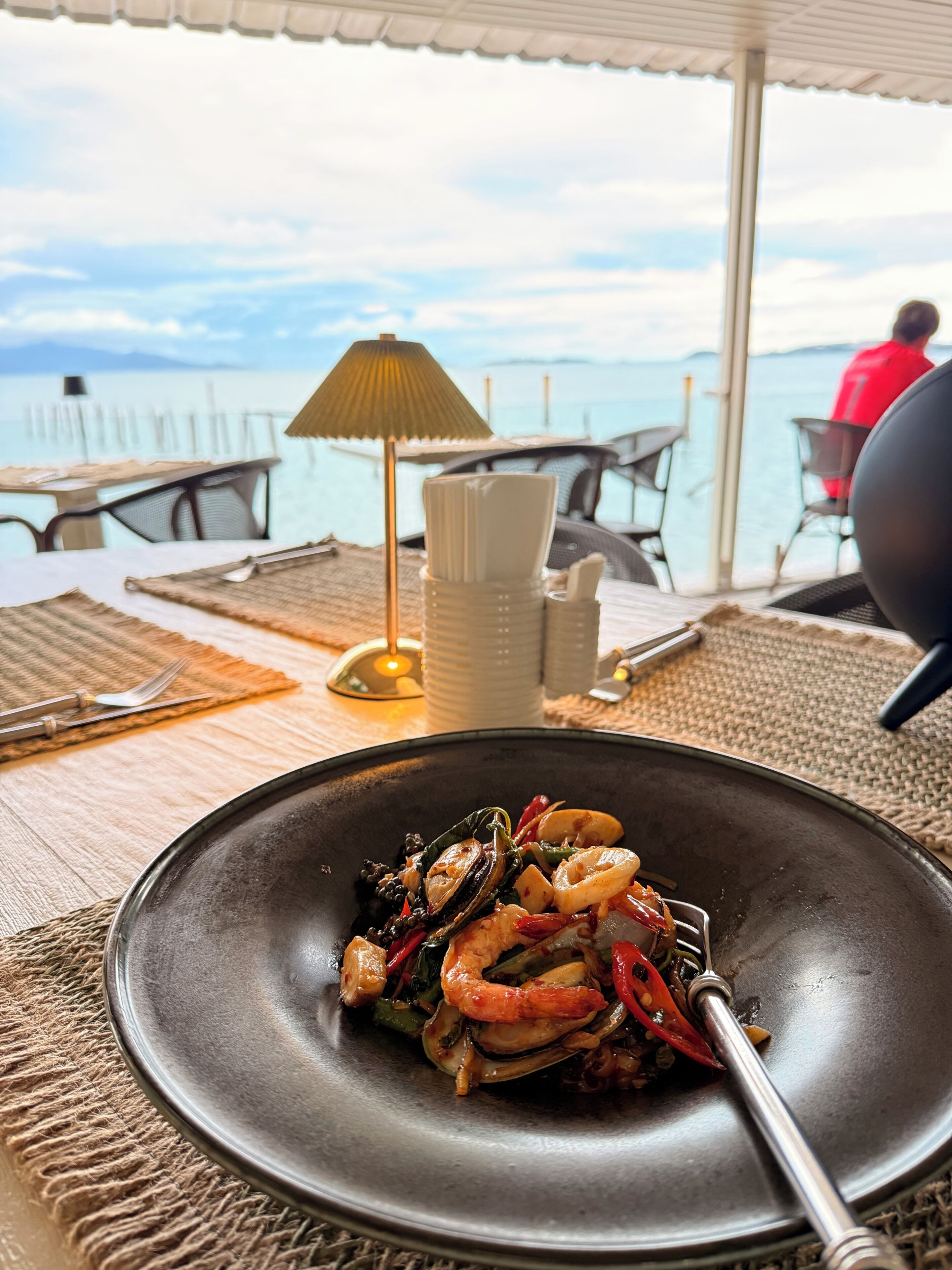 A dining table with a seafood dish, a lamp, and a view of the sea.