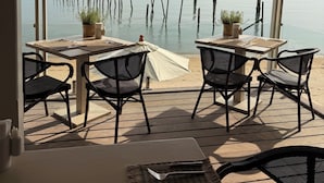 Un área de comedor al aire libre con mesas y sillas, con vistas a una masa de agua tranquila y postes de madera.