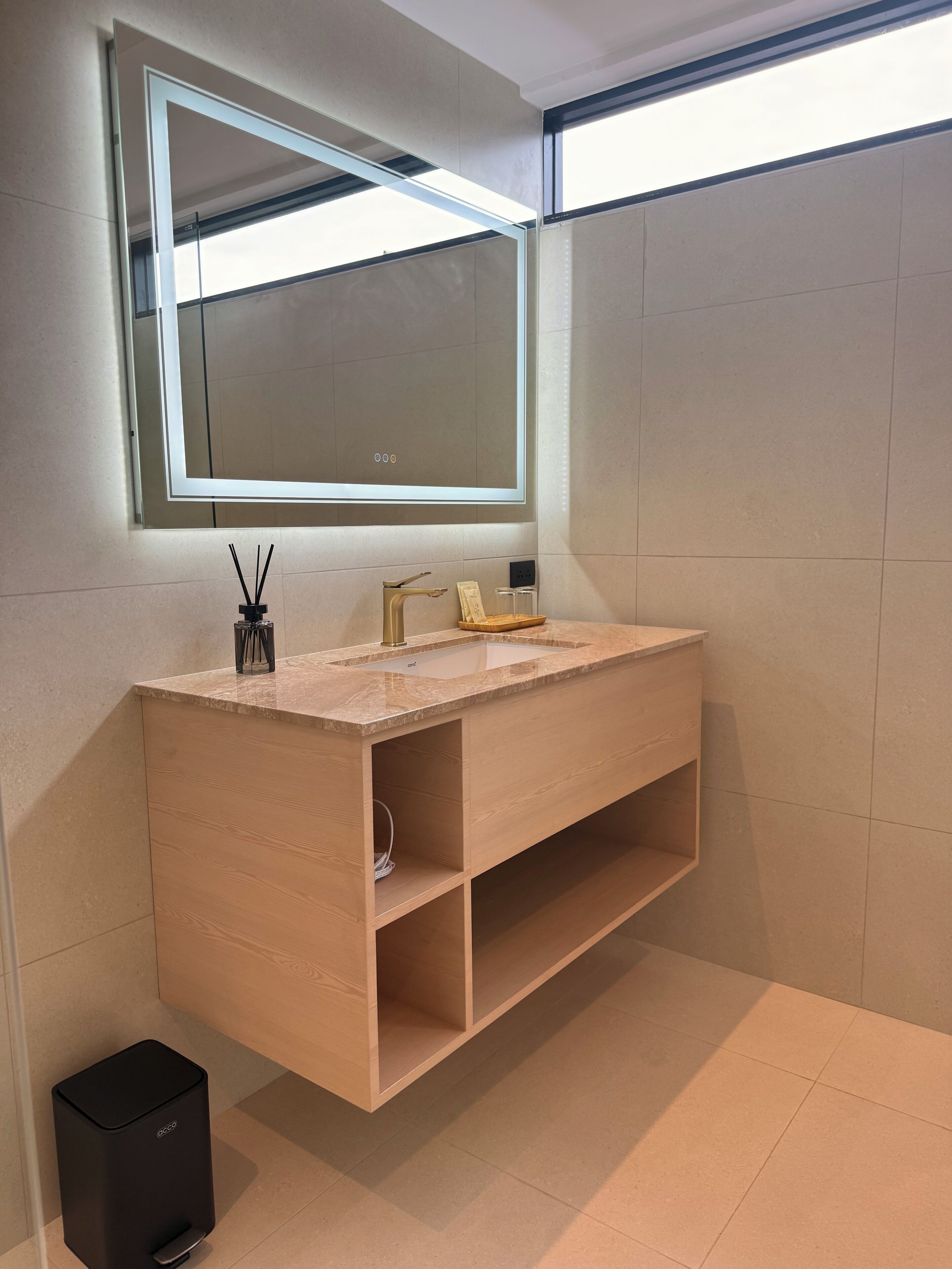 Un baño moderno con un espejo grande, un tocador de madera y un cubo de basura.