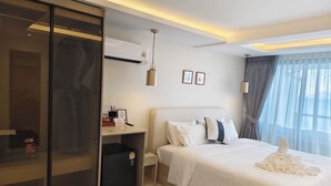 Una habitación de hotel con cama, armario, escritorio y ventana con cortinas.