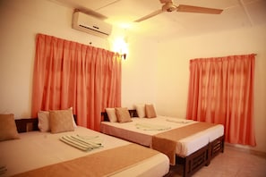 Une chambre d’hôtel avec deux lits simples, un ventilateur de plafond, un appareil de climatisation et des rideaux orange.