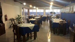 A restaurant with tables set for dining, large windows offering a view of the sea, and a fire extinguisher on the wall. - Hotel Residencias Varadouro (Horta)