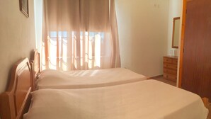 A double bed with a white bedspread in a room with a wooden headboard, a wooden dresser, and a door. - Hotel Residencias Varadouro (Horta)