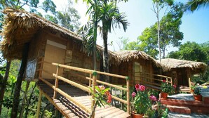 Eine rustikale Holzhütte mit einem Reetdach, einer Holztreppe und einem kleinen Garten mit Blumentöpfen und Blumen.