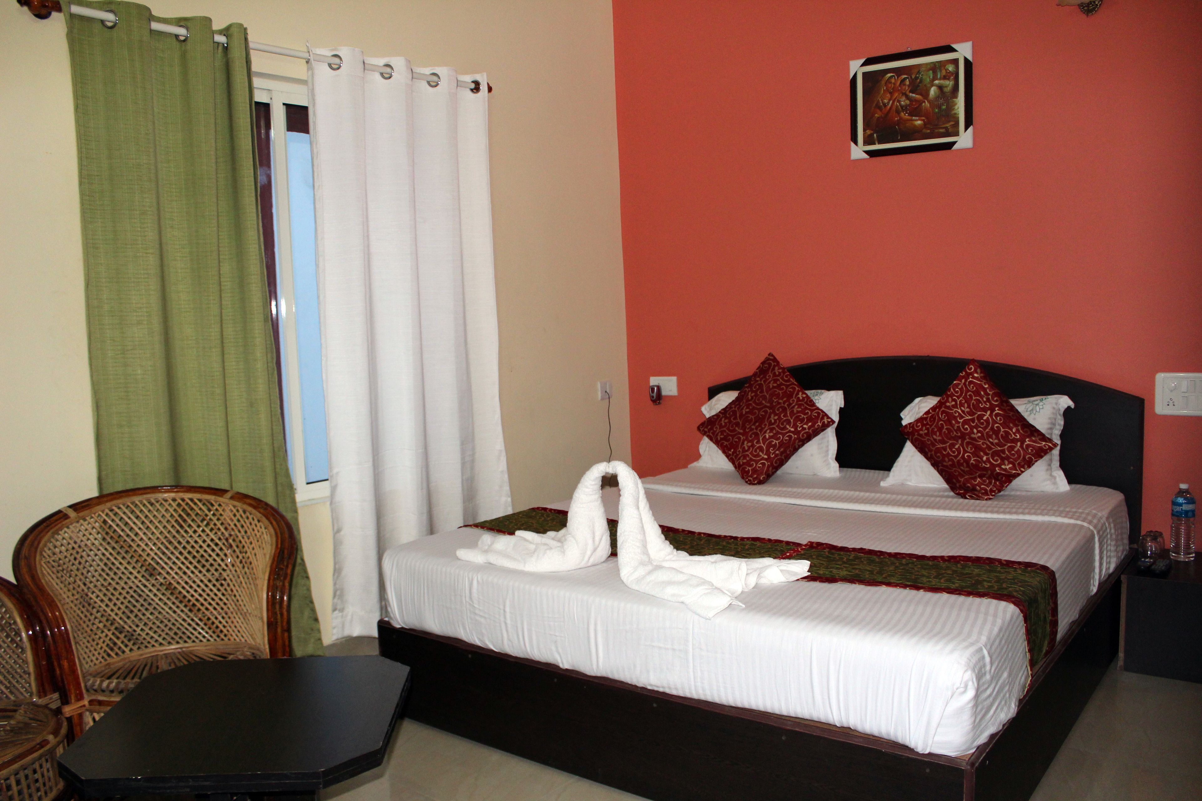 A hotel room with a bed, a chair, a table, and a window with curtains.
