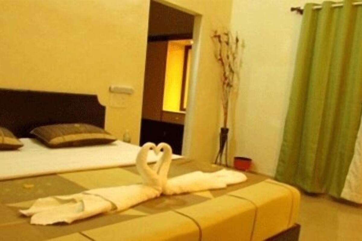 Una habitación de hotel con una cama, almohadas, una escultura de toallas, una cortina verde y un jarrón con ramas.