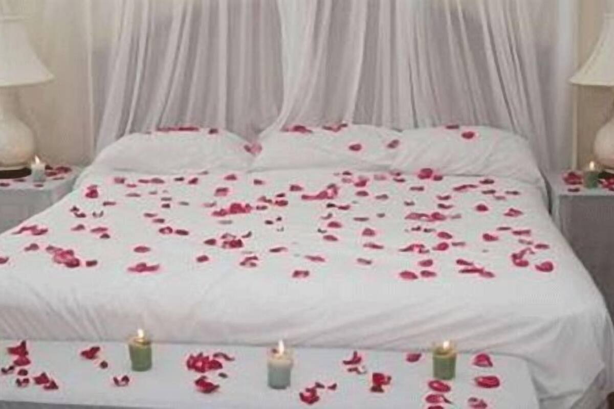 Una cama con pétalos de rosa y velas, un edredón blanco y dos lámparas de noche.