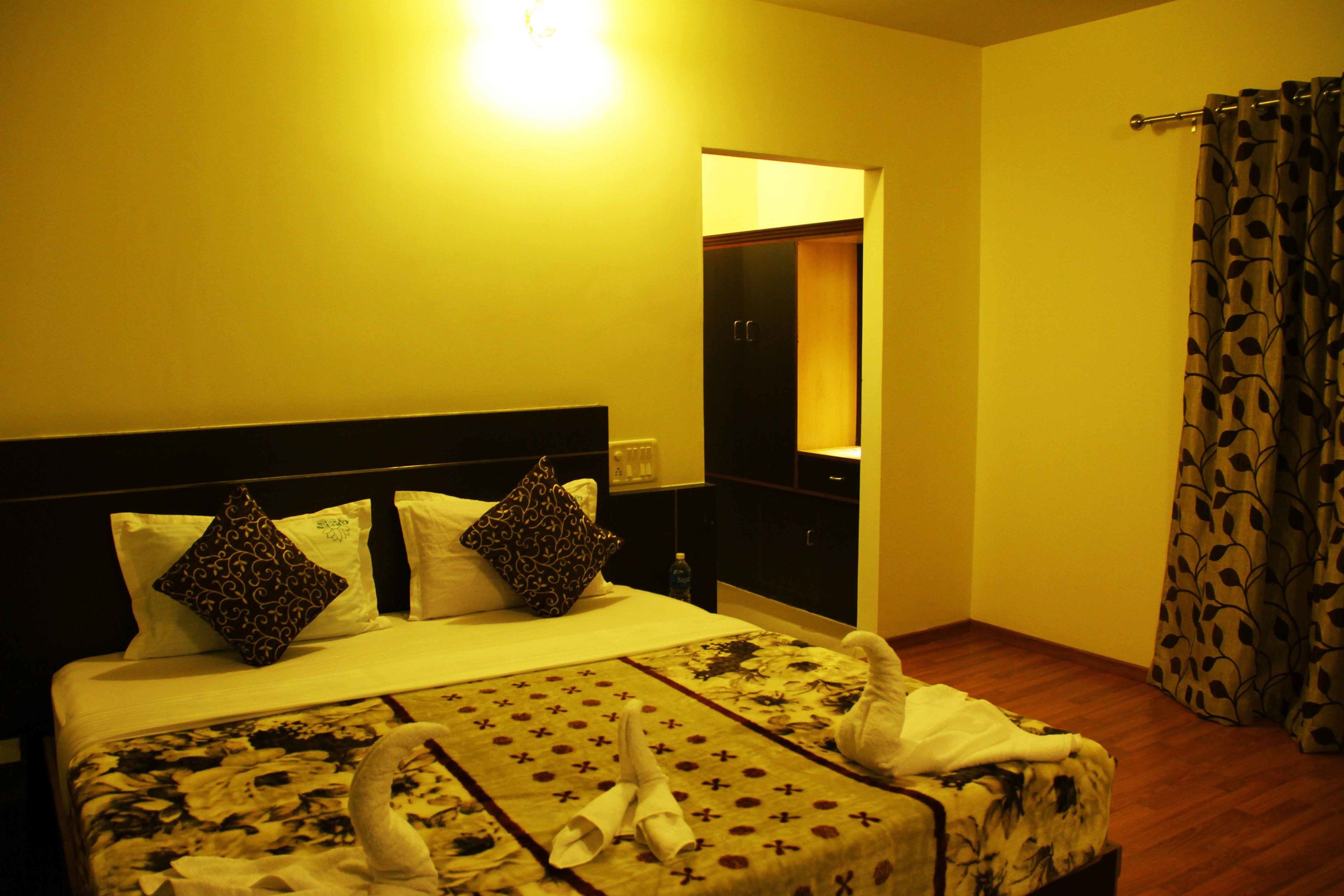 A hotel room with a bed, pillows, a nightstand, a mirror, and a curtain.